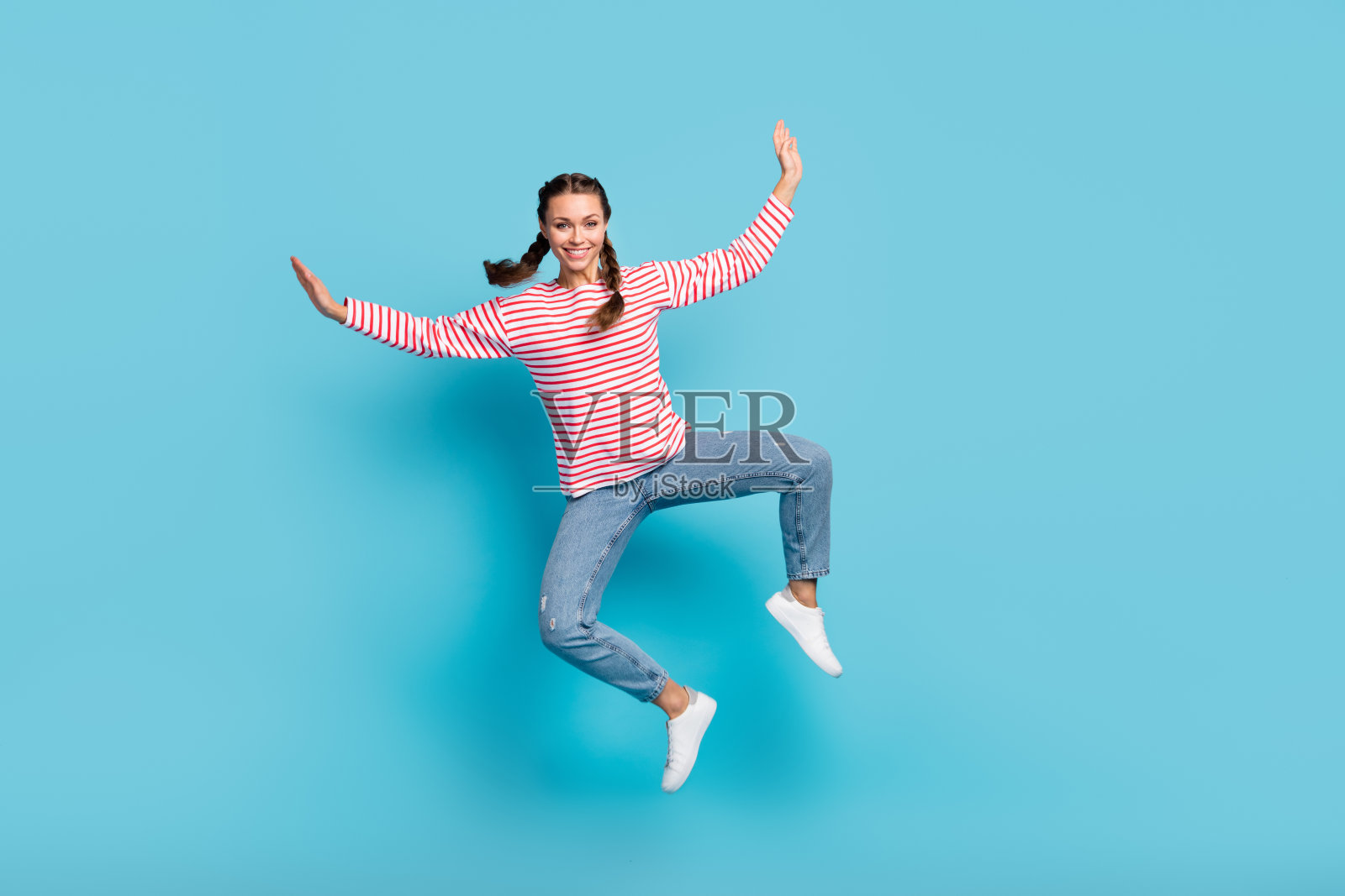 全身照时髦无忧无虑的年轻女士穿红色衬衫跳跃的手臂两侧孤立的蓝色背景照片摄影图片