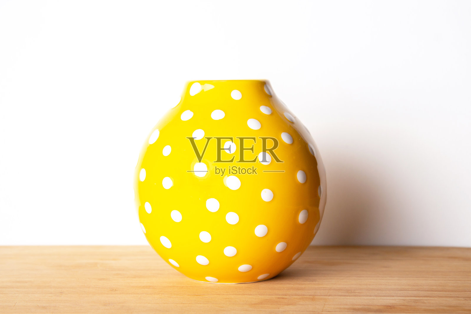 亮黄色花瓶，白色背景上点缀着小圆点照片摄影图片