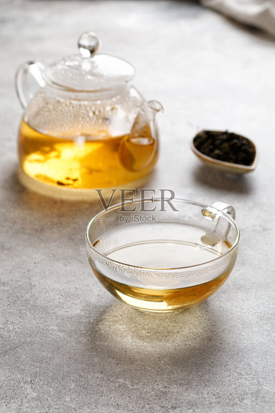 一个有绿色草本茶的马克杯或茶杯和一个茶叶在灰色背景上的茶壶。美丽的颜色照片摄影图片