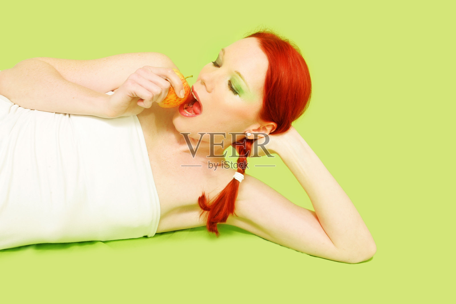 在绿色背景上咬苹果的女人照片摄影图片