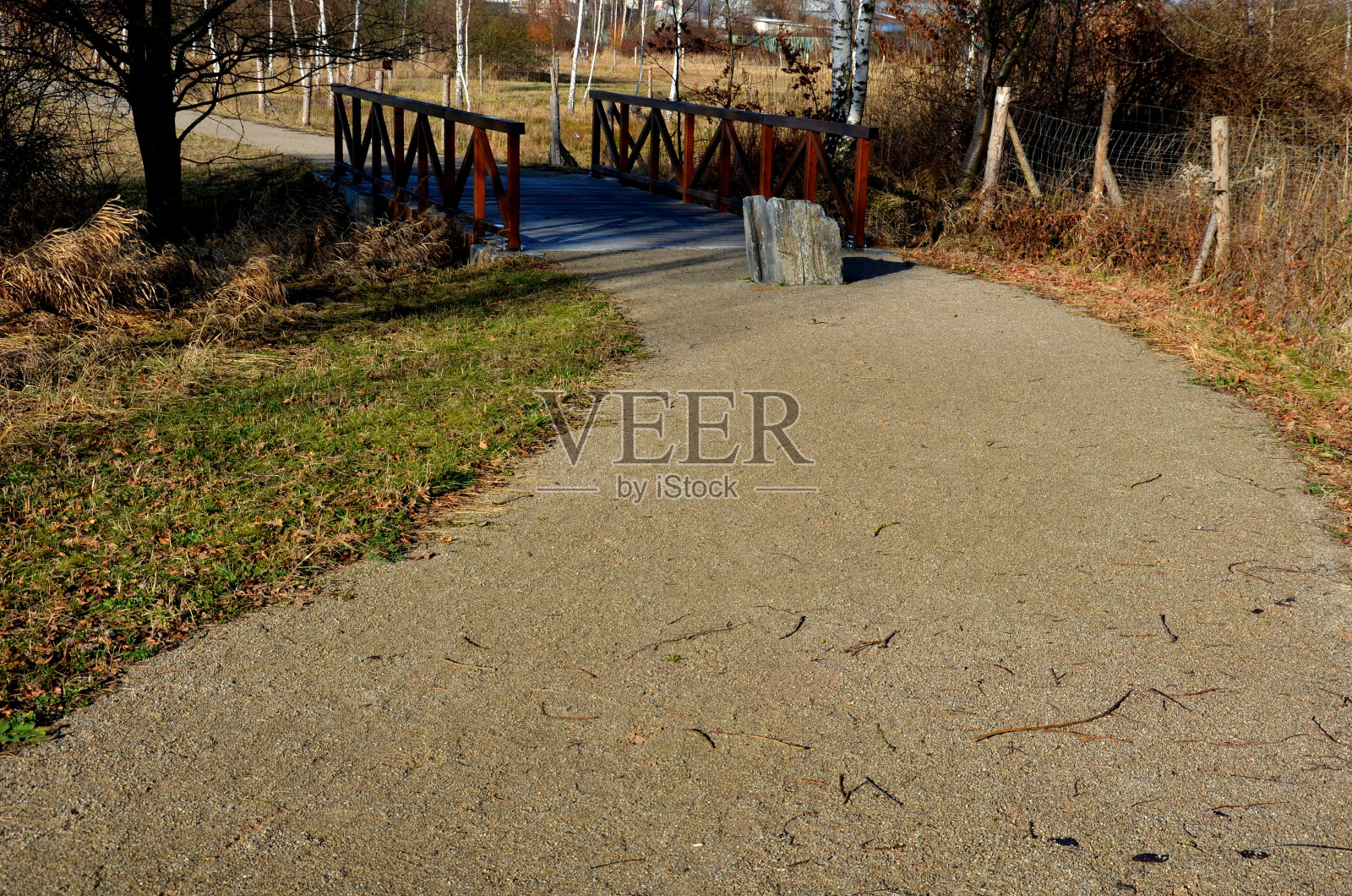 一座有木栏杆的公园桥横跨小溪。这些梁被固定在一根支撑混凝土基础的钢横梁上。路由碎石，桥头前障照片摄影图片