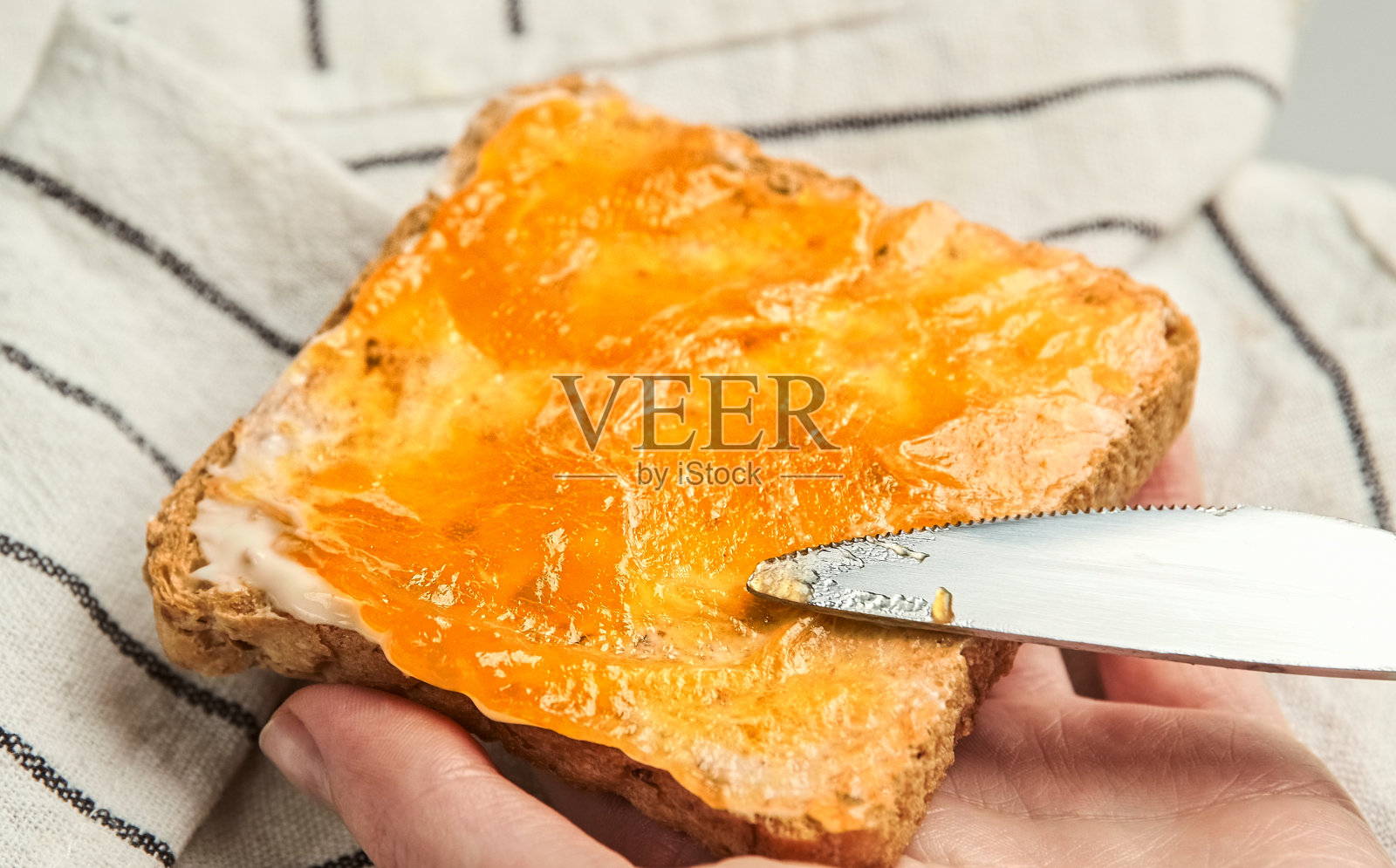 把果酱涂在切片面包上。准备美味的早餐吐司照片摄影图片