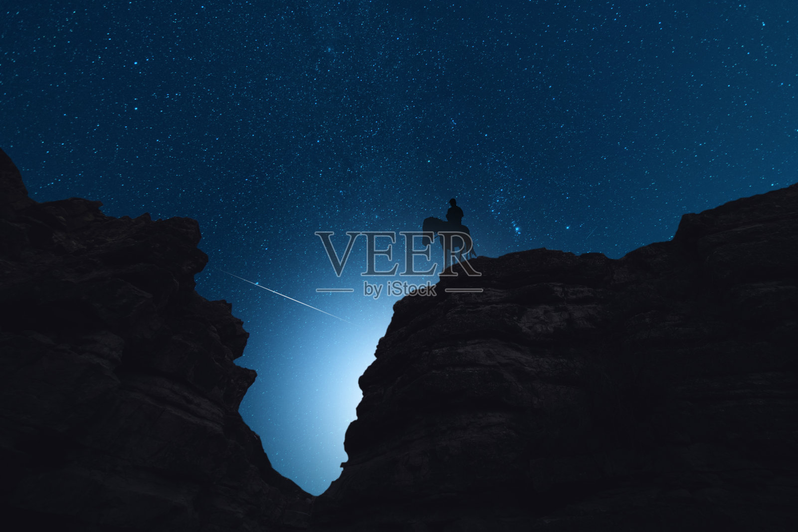 星夜里，独自骑马的人站在岩石上的剪影。他身后是美丽的夜空。照片摄影图片