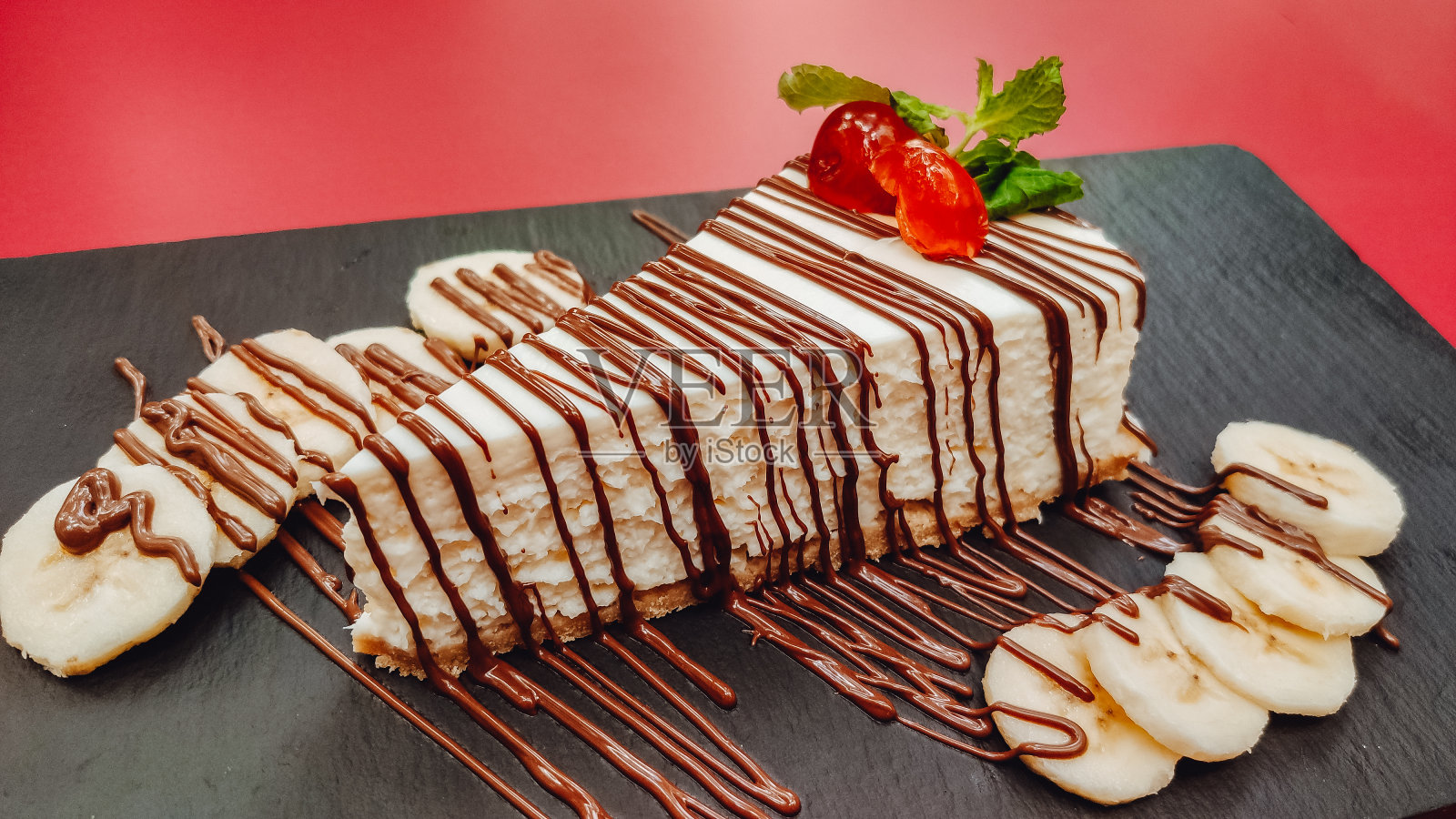 一个美味的自制奶酪蛋糕与巧克力和水果在石板和红色背景的特写视图。烹饪甜点和派的概念照片摄影图片