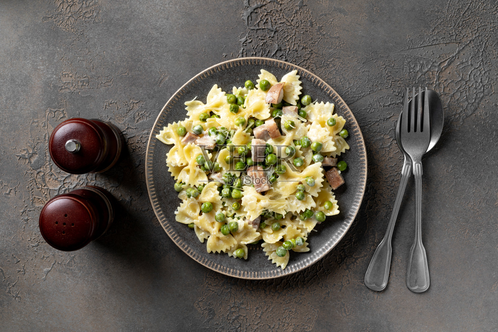 在厨房桌子上的盘子里放着绿豌豆、火鸡火腿和奶油干酪。传统的意大利面在黑暗的烹饪背景。俯视图照片摄影图片