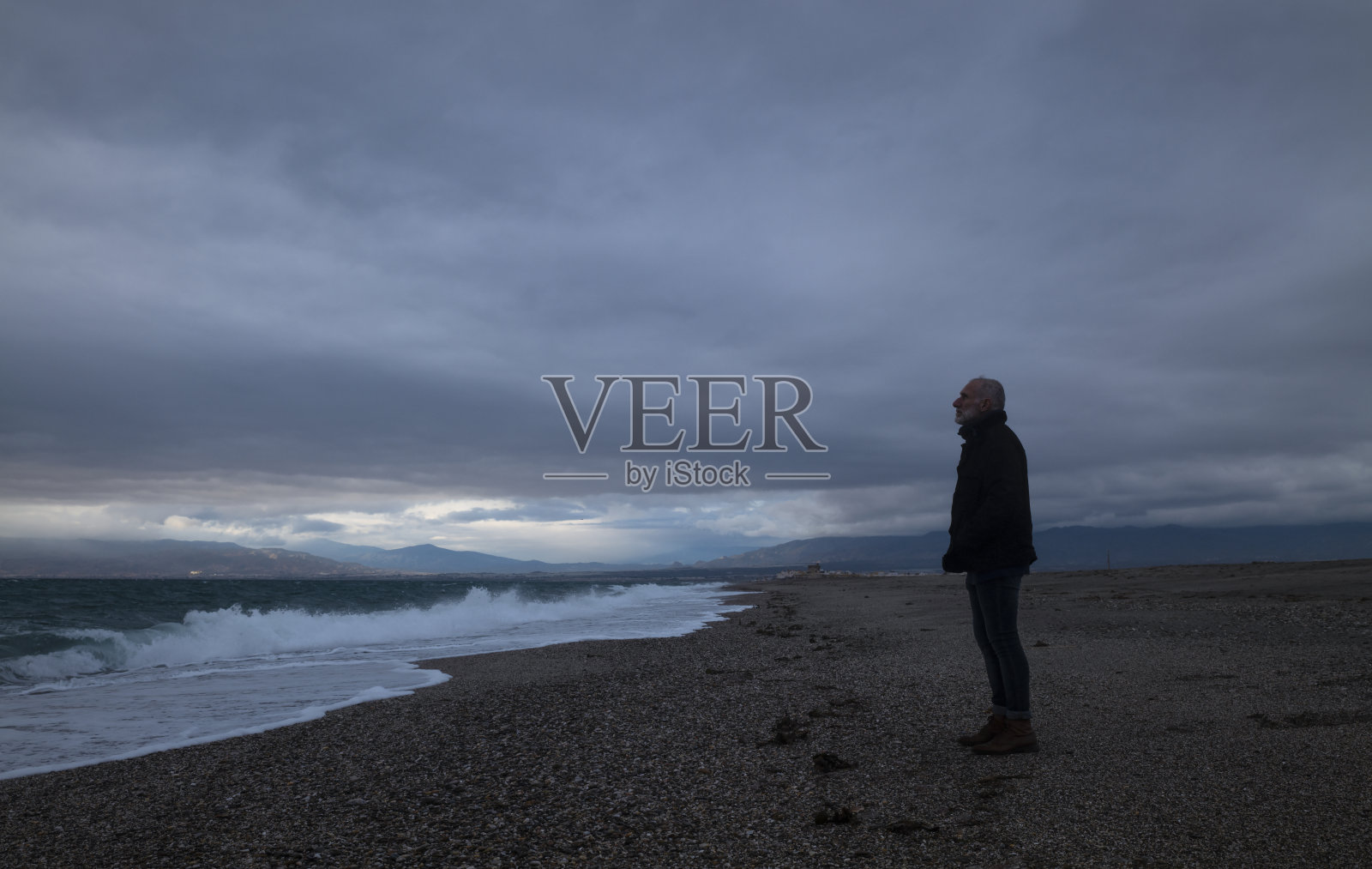 夕阳西下的海滩上，一个穿着冬装的成年男子。西班牙阿尔梅里亚照片摄影图片