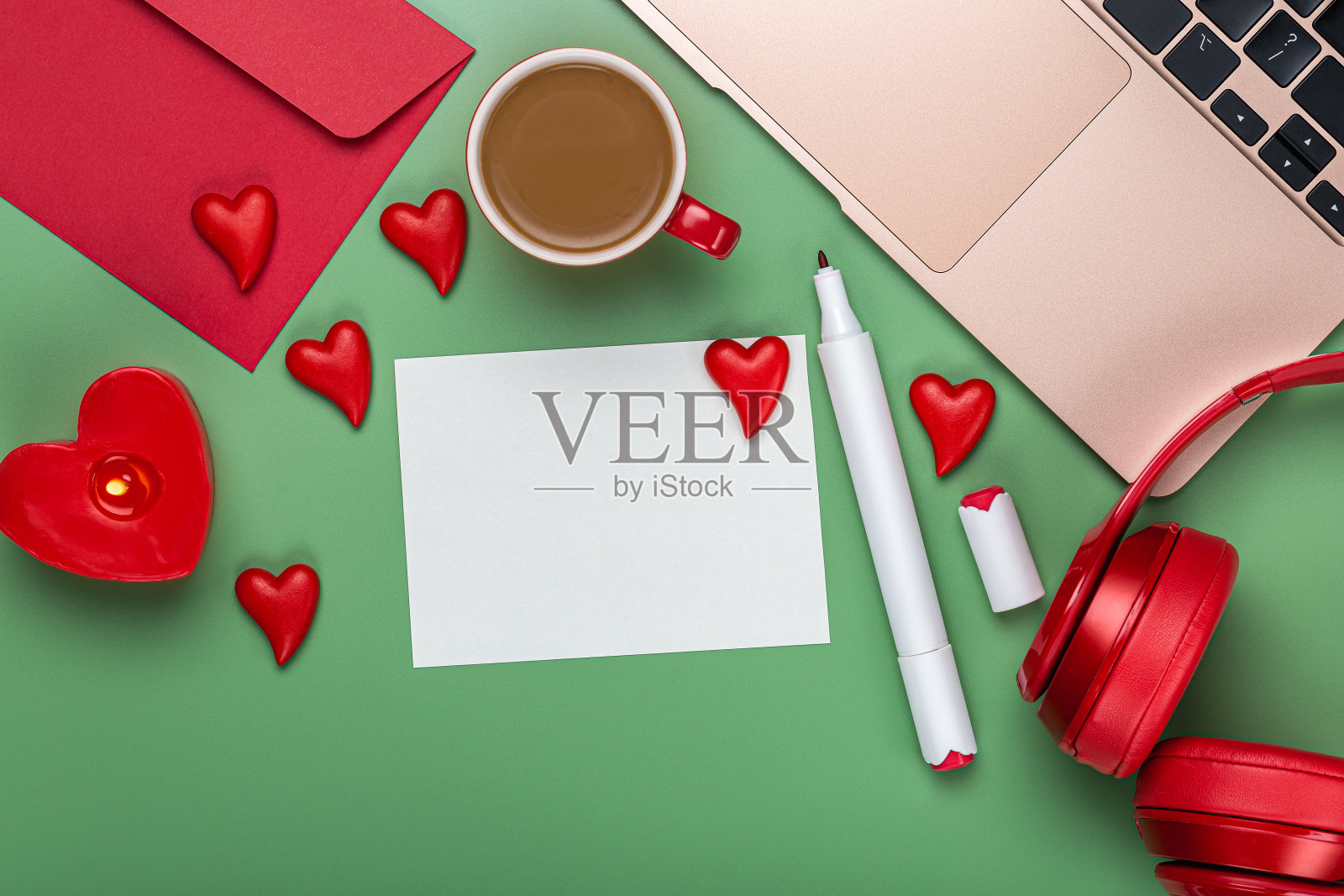 爱的主题。写信的项目。一张白纸，一个红信封，耳机，一支蜡烛，一杯咖啡，一支马克笔，一台笔记本电脑和绿色桌面背景上的许多爱心。情人节照片摄影图片