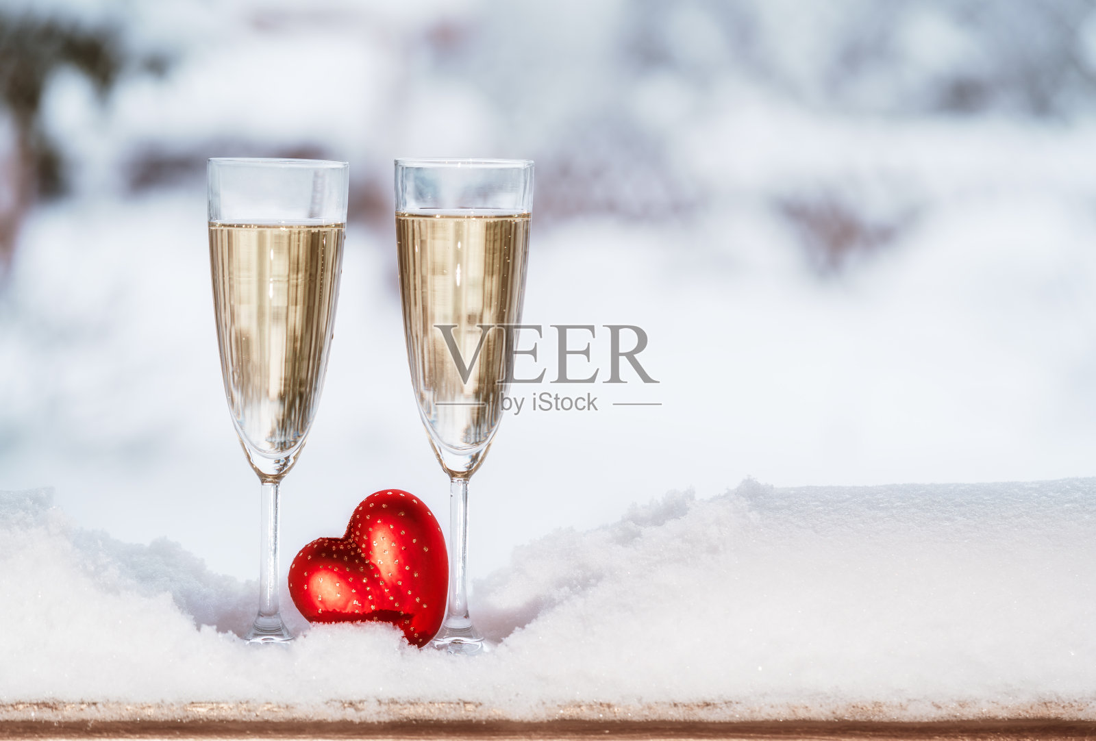 特写的两个香槟长笛冷却在雪和红色的心在冬天的自然背景。照片摄影图片