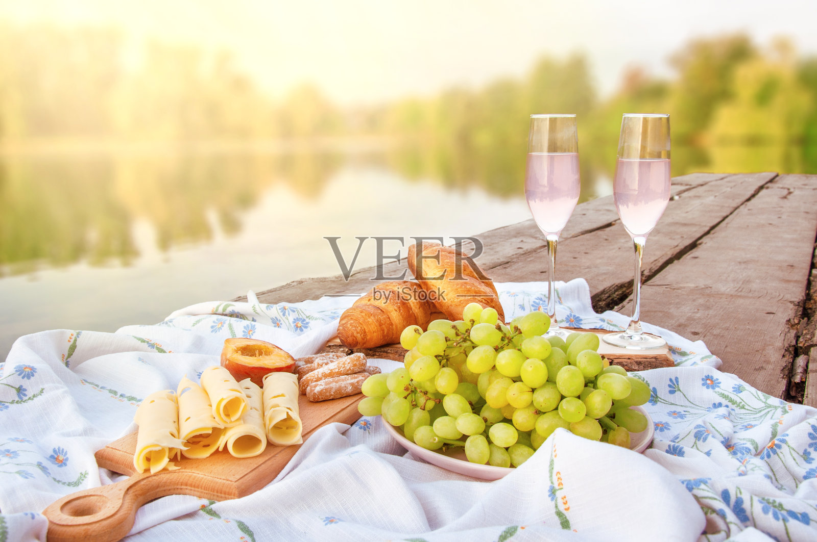 在河边的木桥上进行浪漫的野餐，有香槟、水果、糕点和奶酪。放松照片摄影图片