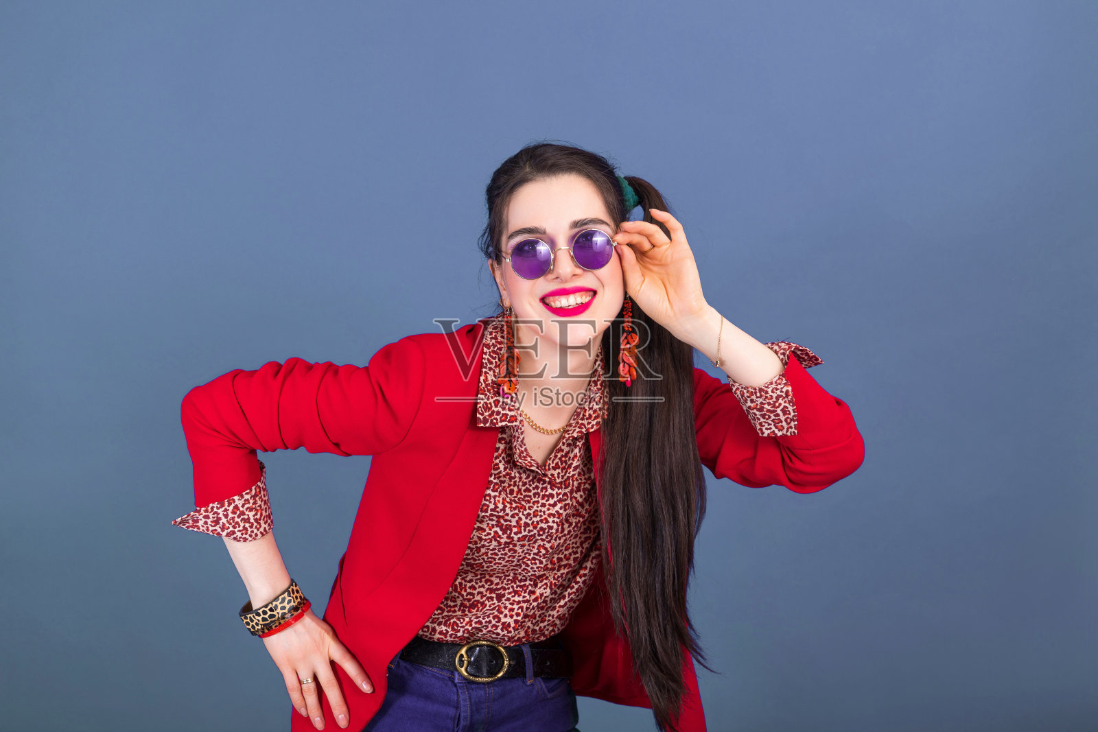 快乐微笑的年轻黑发女人在90年代风格与蓝色背景圆形太阳镜照片摄影图片