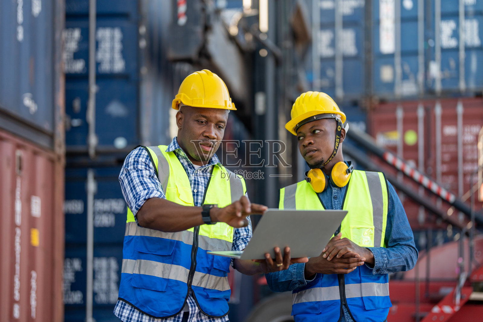 非洲工人、工程师、技术人员手持笔记本电脑，检查现场集装箱区域的运输和机器吊装情况。概念人操作在重工业。照片摄影图片