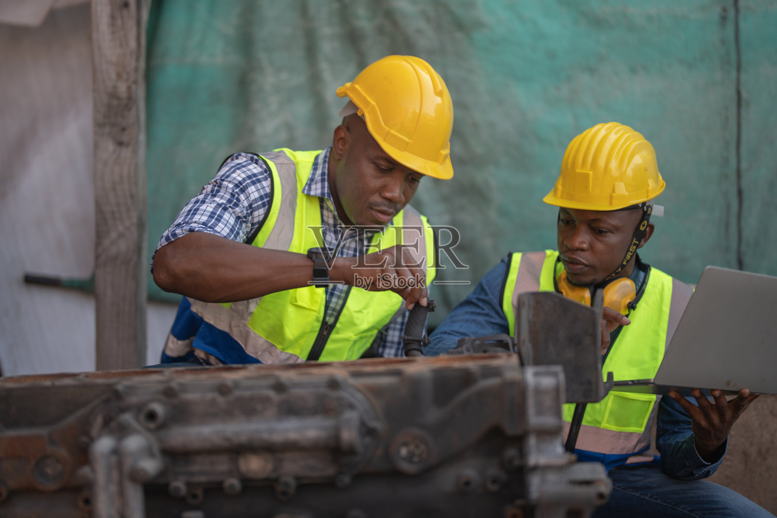 非洲工人、工程师、技术员手持手提电脑检查重型机械发动机。修理重工业机械零件的工头。照片摄影图片