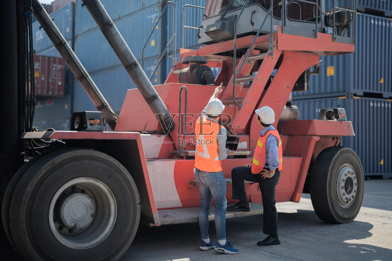 工厂工人、工人、工人站在仓库的集装箱前。工人在重型机械车辆前检查和会议。照片摄影图片