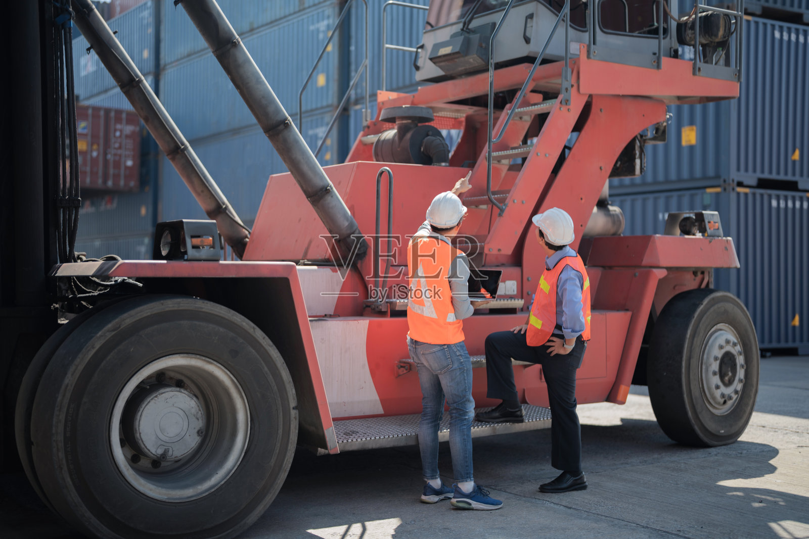 工厂工人、工人、工人站在仓库的集装箱前。工人在重型机械车辆前检查和会议。照片摄影图片
