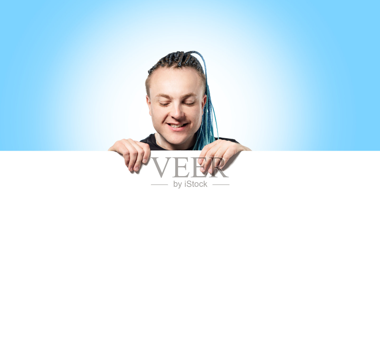 一个留着有趣的莫霍克发型的年轻人从一堵白墙上方向外张望。墙上有写字的地方照片摄影图片