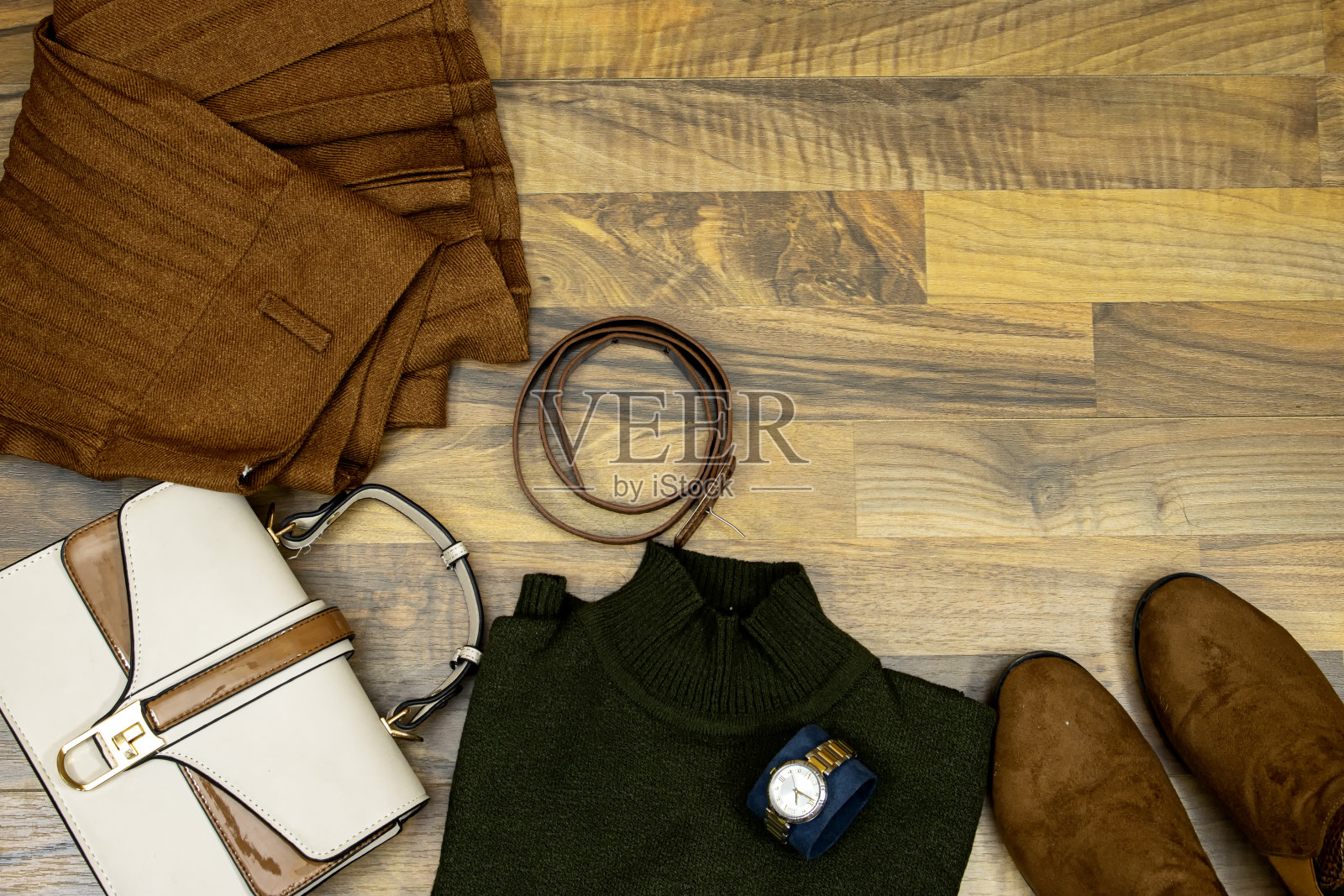 一套时髦的衣服和饰品。绿色毛衣和波纹裙，手提包，短靴和棕色皮带在木桌子上，平躺。在趋势照片摄影图片