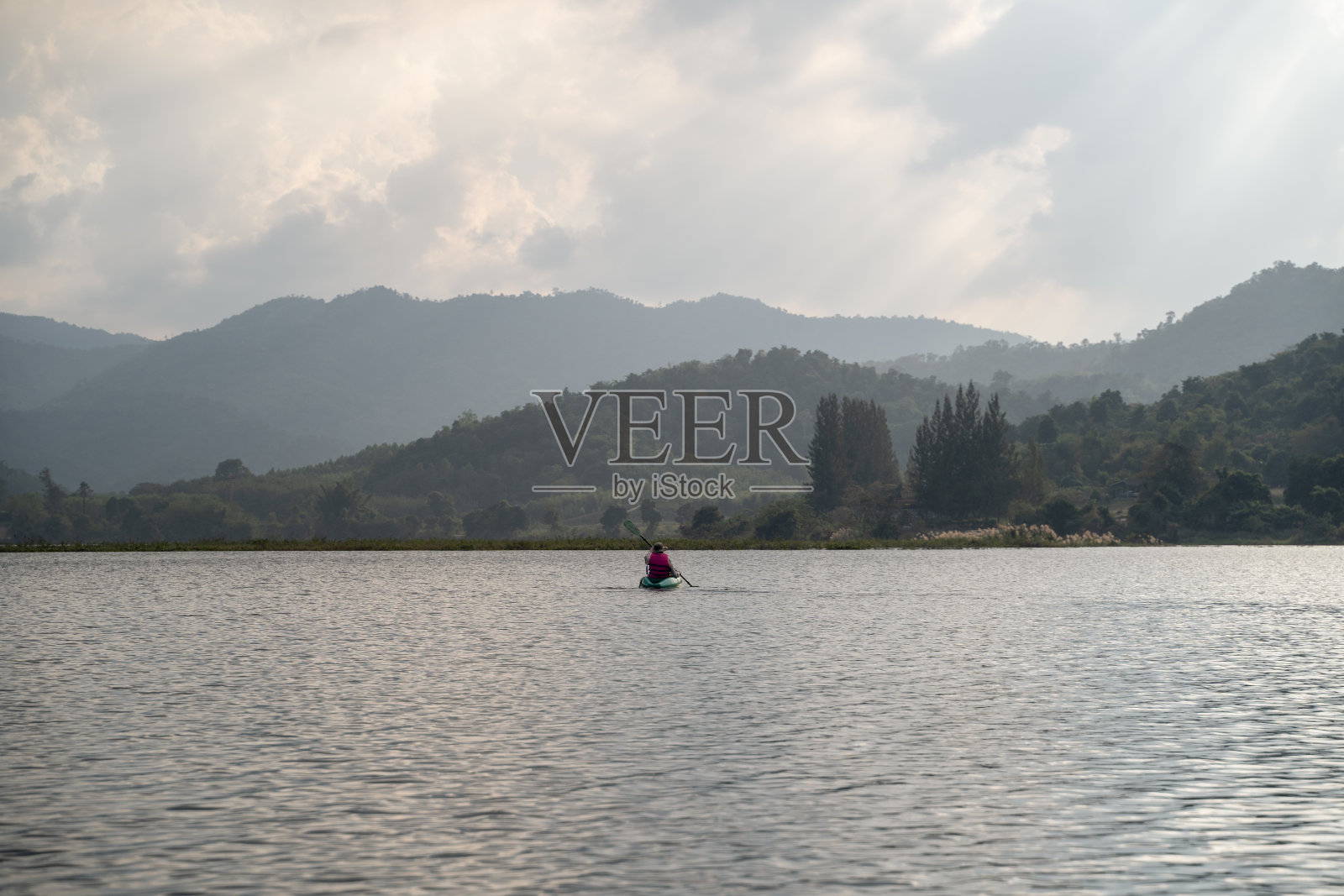 在湖里划皮艇。游客在镜湖上划皮艇。旅游活动时拍照。夕阳下，女子在水中嬉戏。活跃的女子划船在湖与山景在晚上。照片摄影图片
