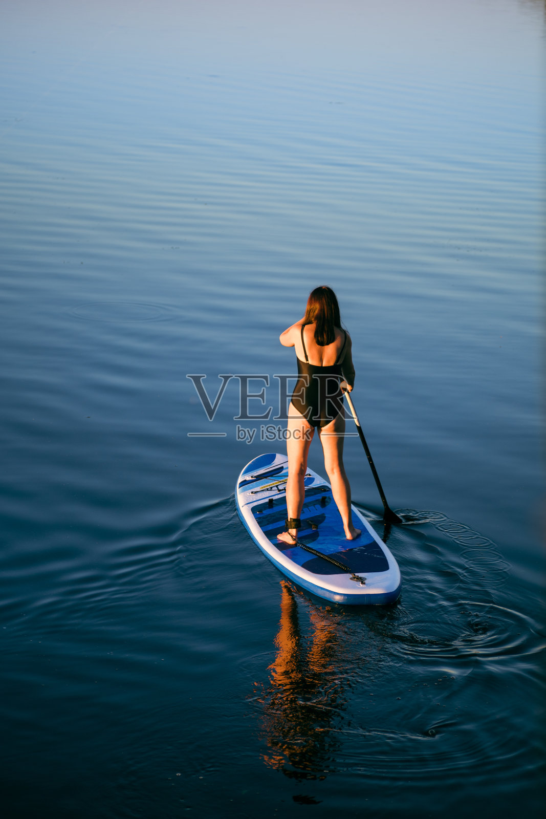 从上面的后视图高加索妇女上船与水晶蓝色的水与清晰的镜子反射在水在晚上的时间。积极的生活方式照片摄影图片