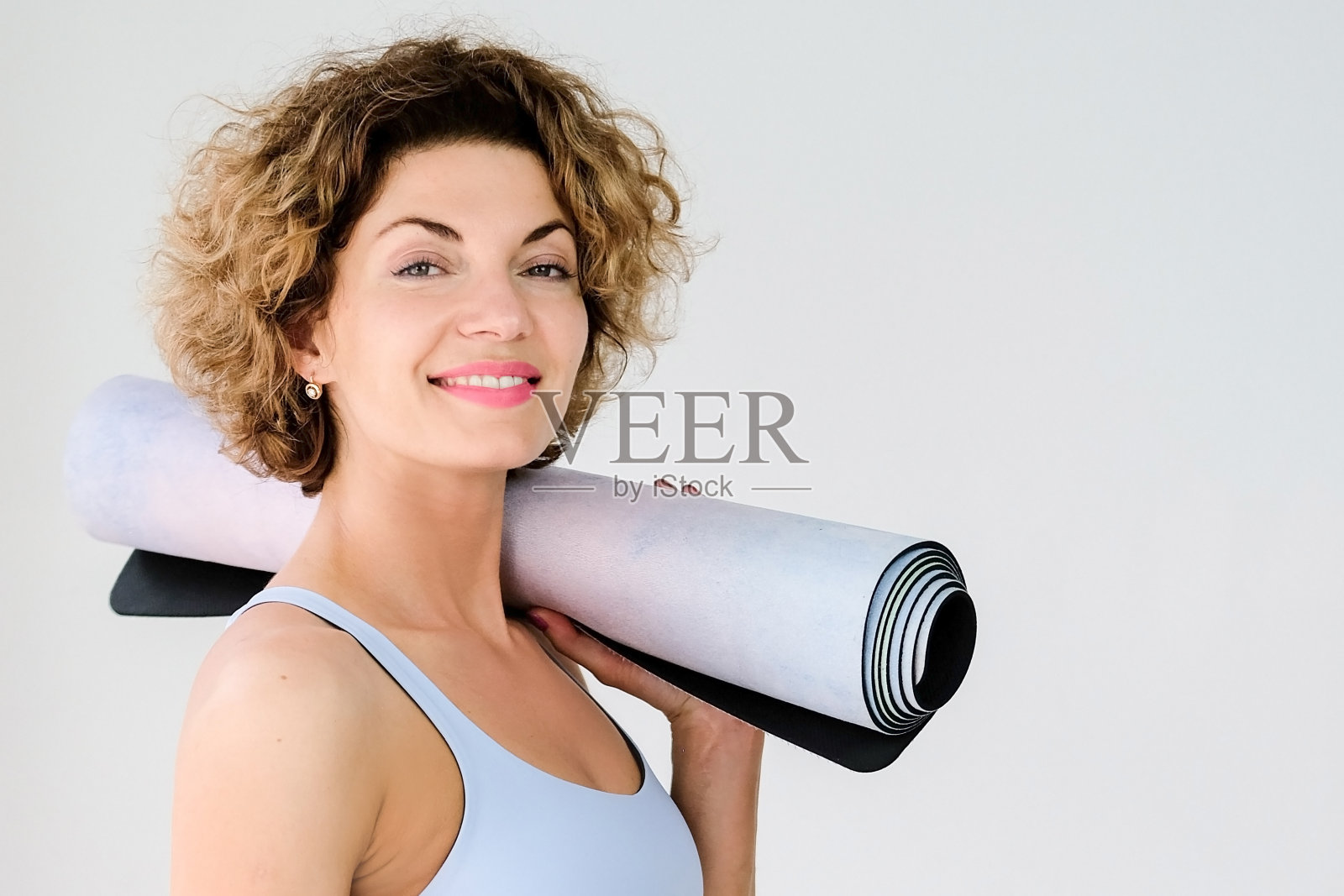 瑜伽运动。一个年轻美丽的女人的肖像与瑜伽垫在她的肩膀上。复制的地方。特写镜头。灰色背景照片摄影图片