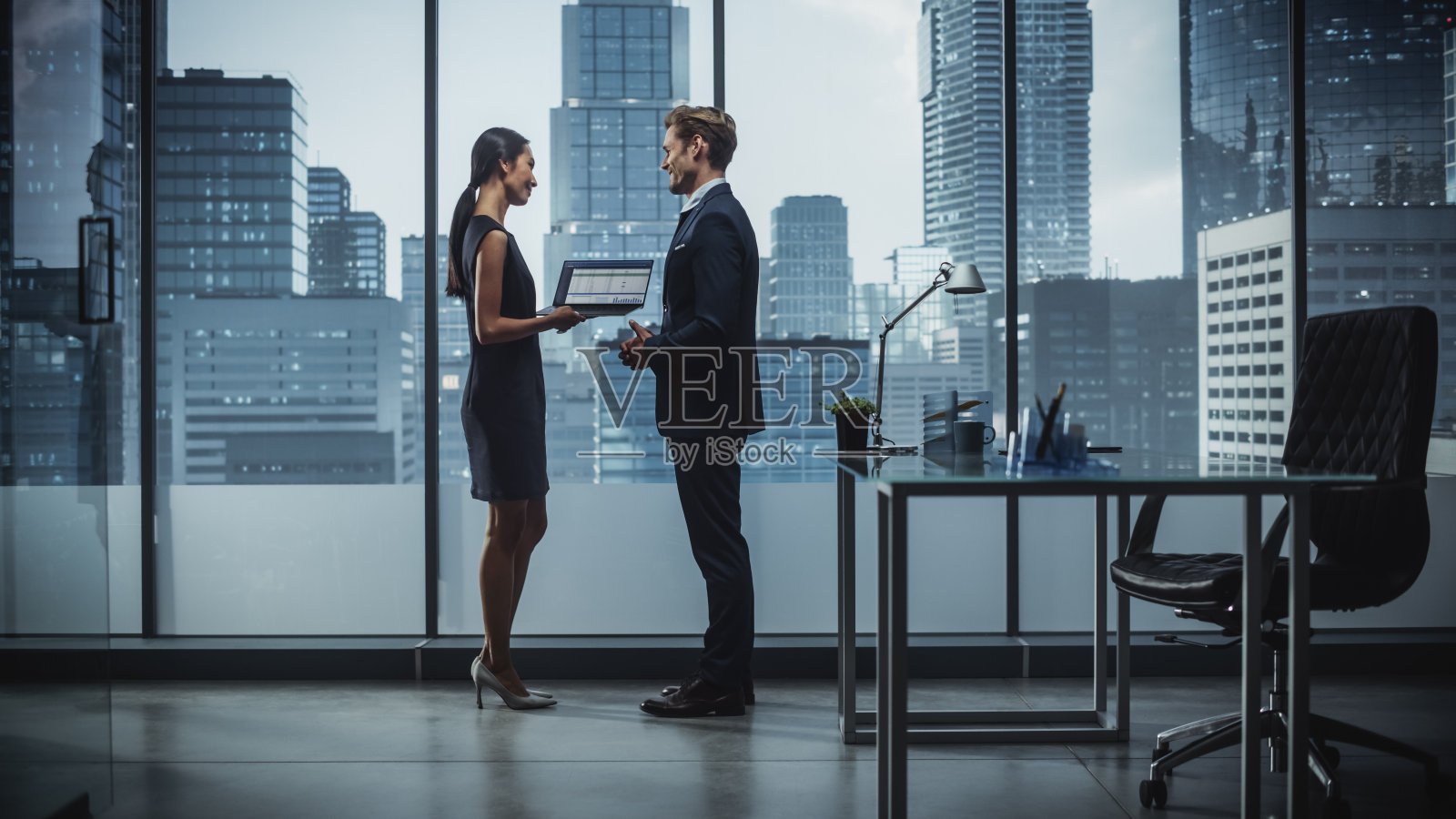 成功的企业首席执行官和投资经理在城市办公室使用笔记本电脑交谈的肖像。两位成功商人就电子商务营销项目进行头脑风暴。照片摄影图片