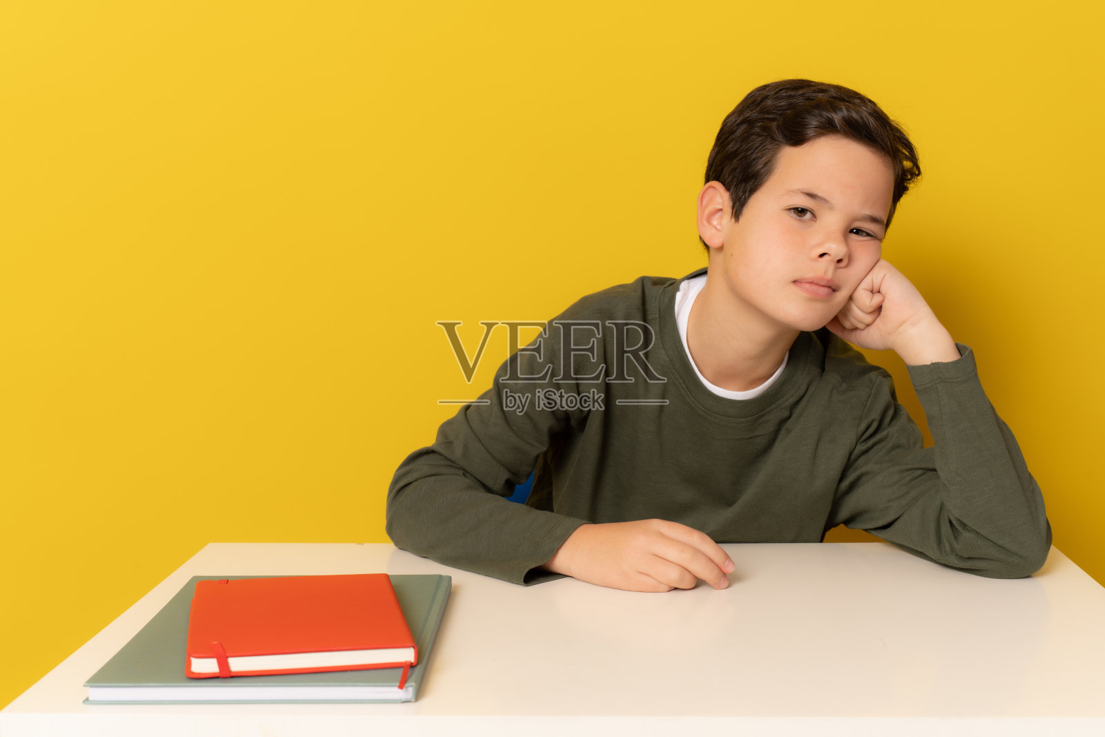 学生无聊的男孩坐在书桌上孤立的黄色背景。照片摄影图片