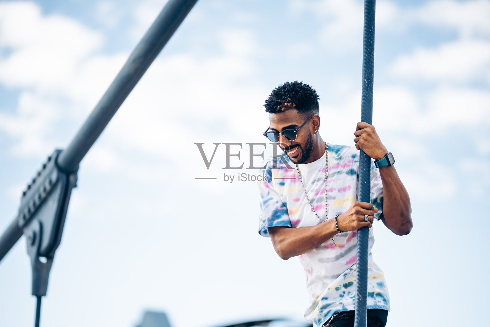 一名戴着太阳镜的黑人戴着墨镜，面带微笑，在连接着桥缆的街道上开心地走着照片摄影图片