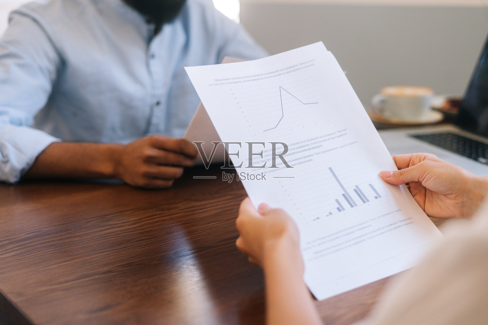 无法辨认的女商人阅读文件坐在桌子旁与男性商业伙伴在办公室。照片摄影图片