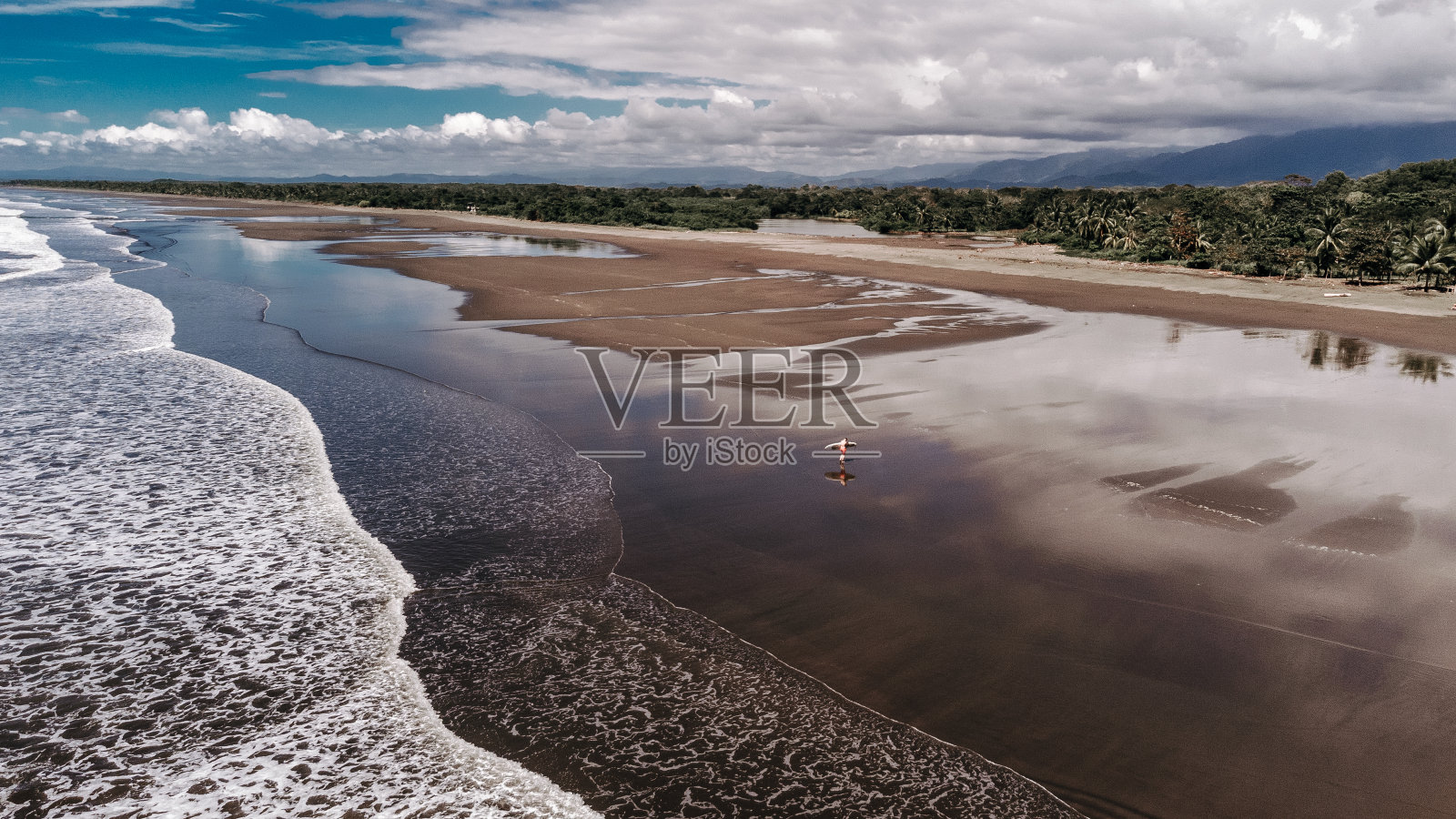 冲浪者漫步在长长的热带海滩上照片摄影图片