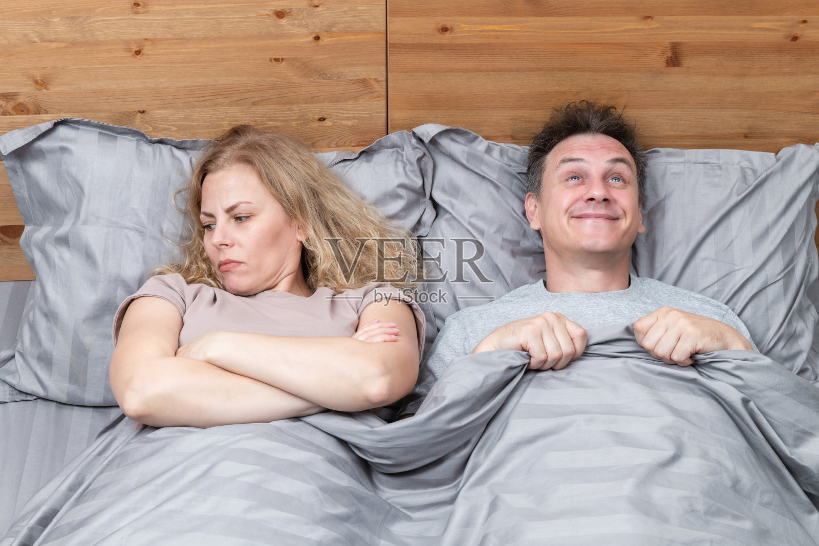 快乐的男人和不满的女人盖着被子躺在床上。关系的概念照片摄影图片