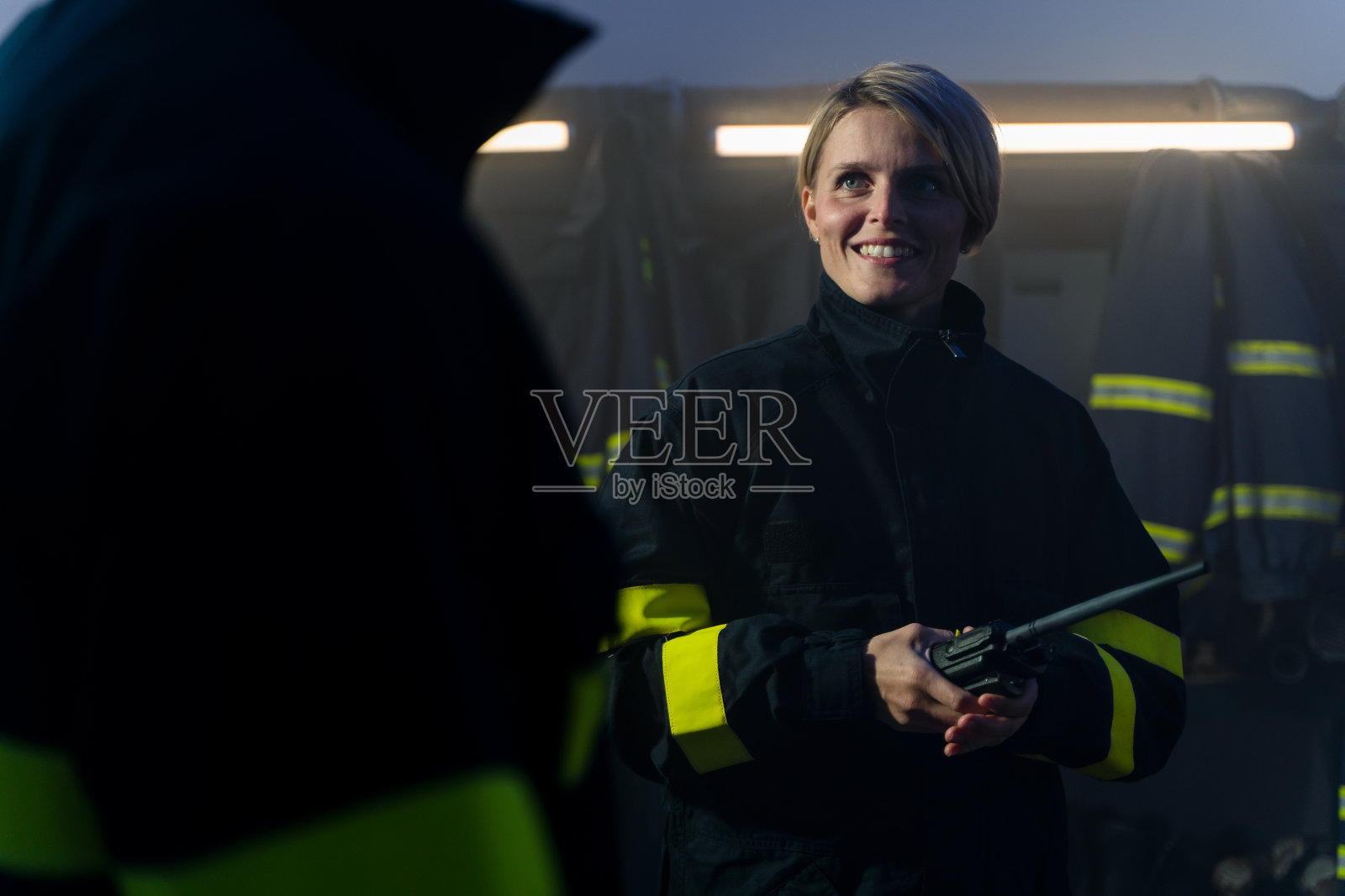 快乐的中年女消防员，带着对讲机在消防站的夜晚。照片摄影图片