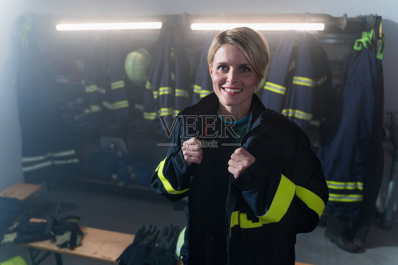 快乐的中年女消防员看着摄像机在消防站的夜晚。照片摄影图片