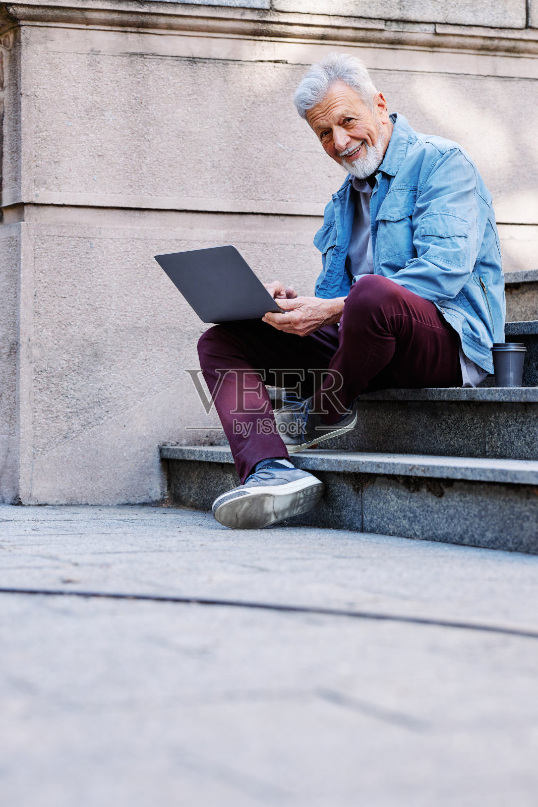 一个快乐的大四学生正坐在大学楼前的楼梯上，手里拿着笔记本电脑学习。再培训的概念。照片摄影图片