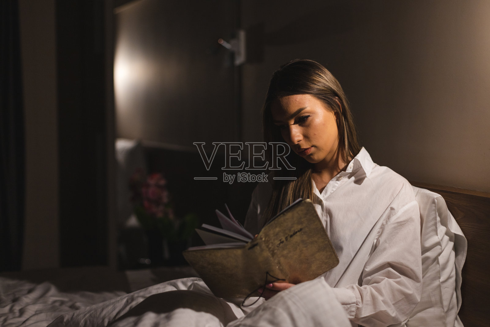 一个年轻漂亮的女人躺在酒店房间的床上，在睡觉前看书照片摄影图片