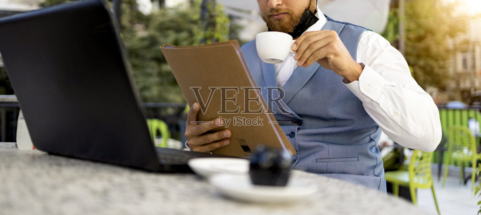 年轻的商人带着防护面罩在路边咖啡店用笔记本电脑拍照照片摄影图片