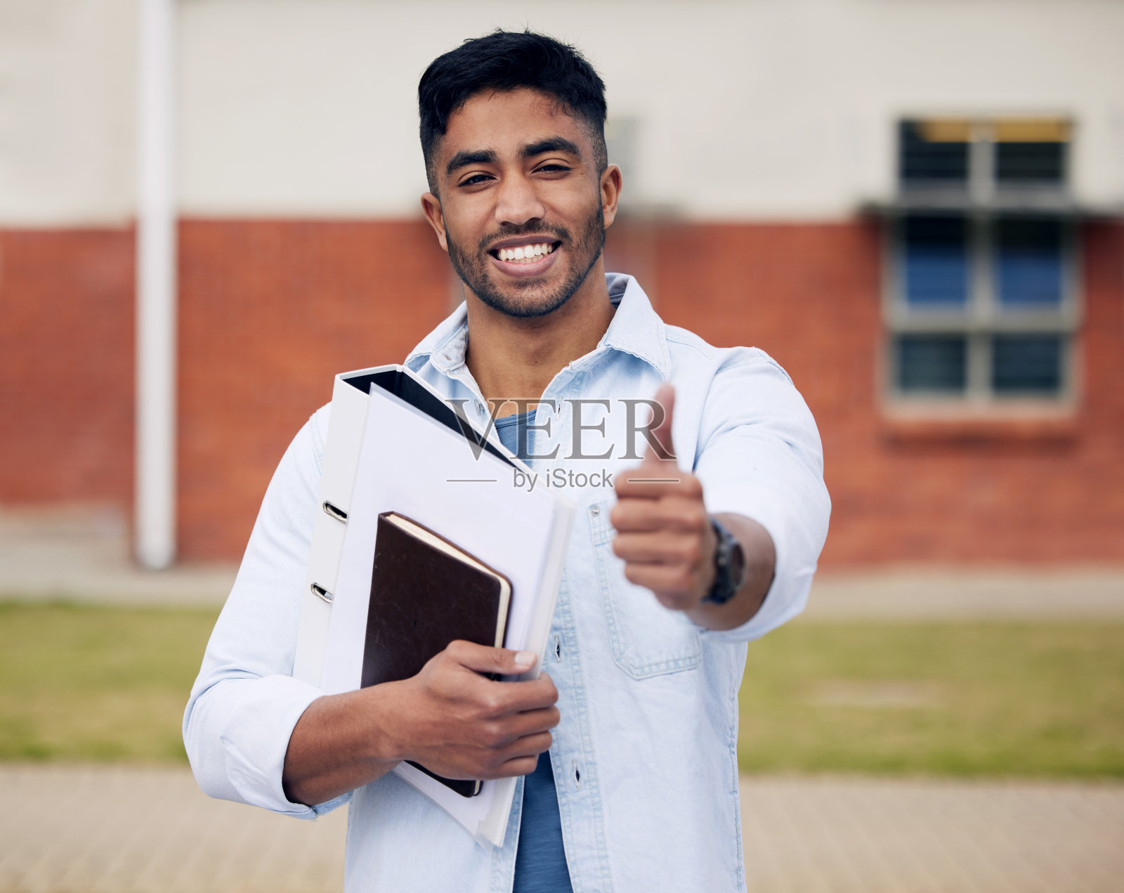 一个年轻人站在大学外面竖起大拇指的照片照片摄影图片