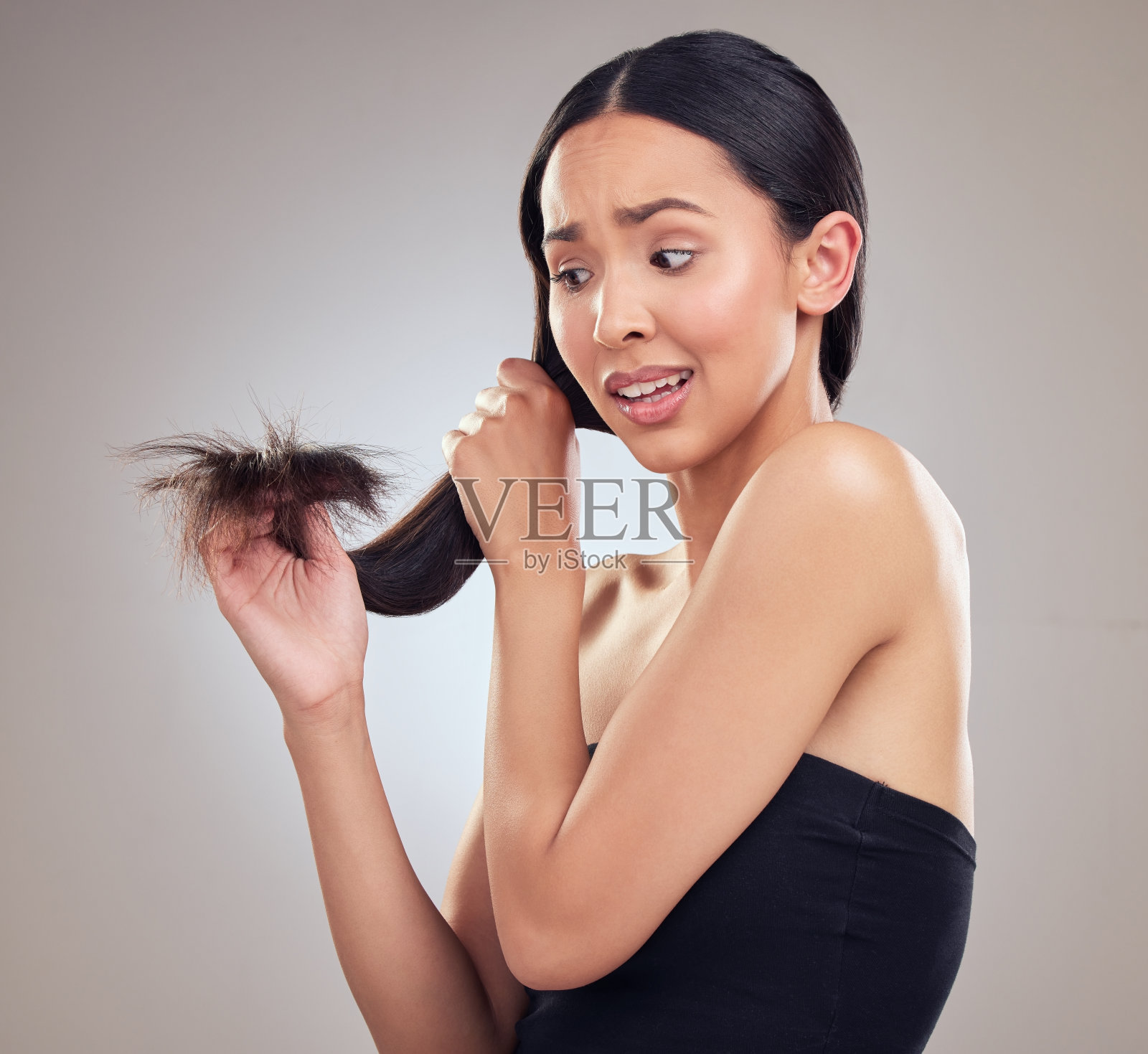 这张照片拍摄的是一位迷人的年轻女子，她拿着头发，看起来很焦虑，在工作室摆姿势照片摄影图片