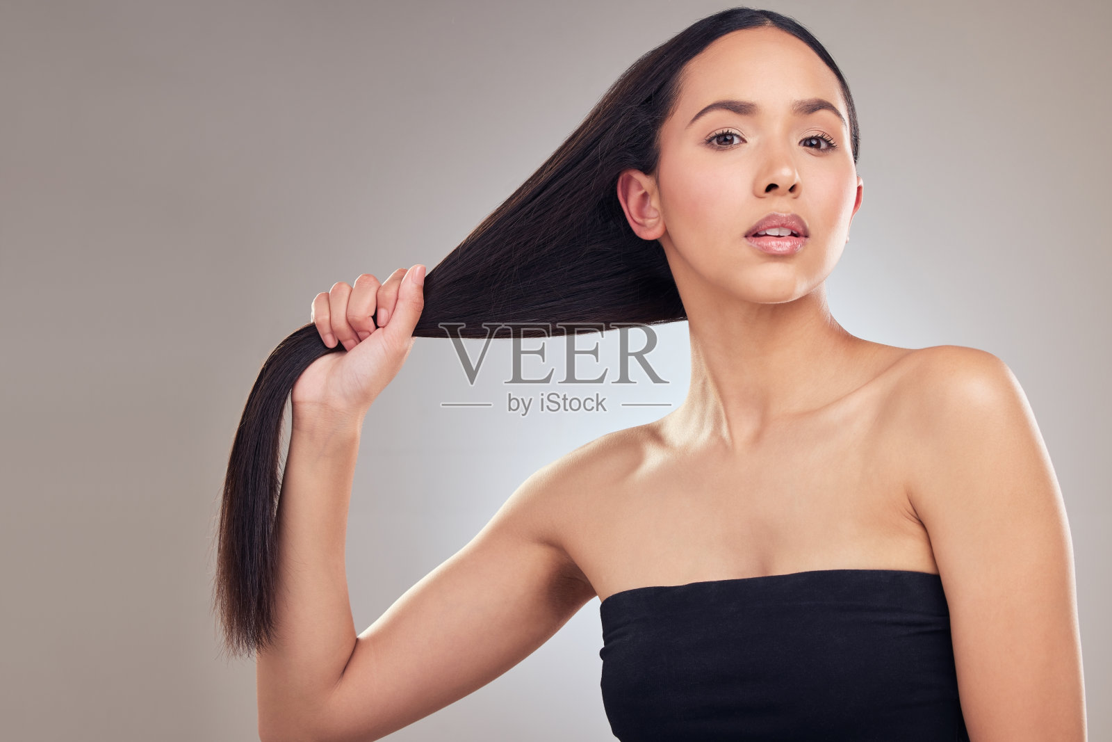 一个迷人的年轻女子独自在工作室摆姿势，握着她的头发照片摄影图片