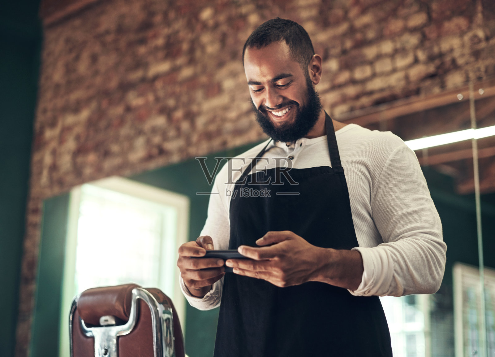 一个年轻英俊的理发师独自站在他的沙龙里用他的手机照片摄影图片