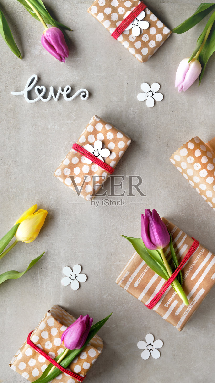春天的背景与郁金香。用牛皮纸包的礼物，爱的话语。浅灰色石头的俯视图。黄色，红色的郁金香，白色的装饰花。春季假期背景与低影响装饰照片摄影图片