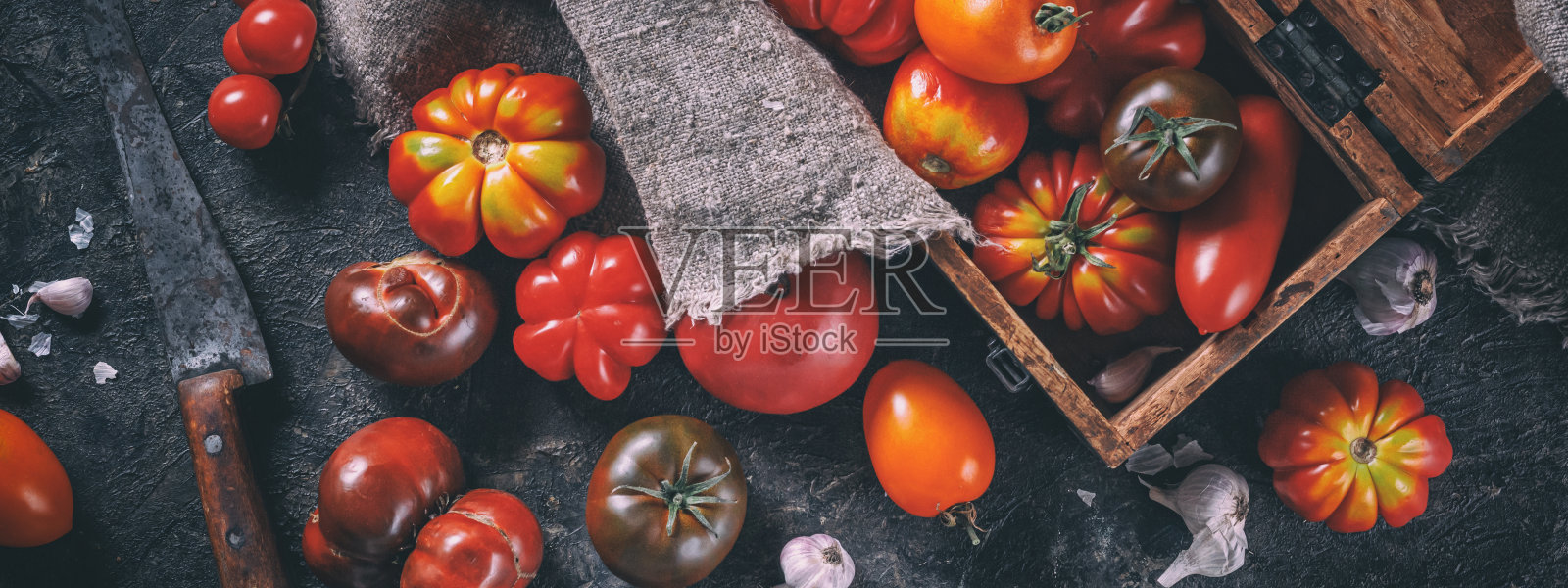 彩色成熟的有机传家宝品种番茄刀和木制盒子上深色的桌子背景，厨房全景，横幅。收获和加工蔬菜的概念。照片摄影图片