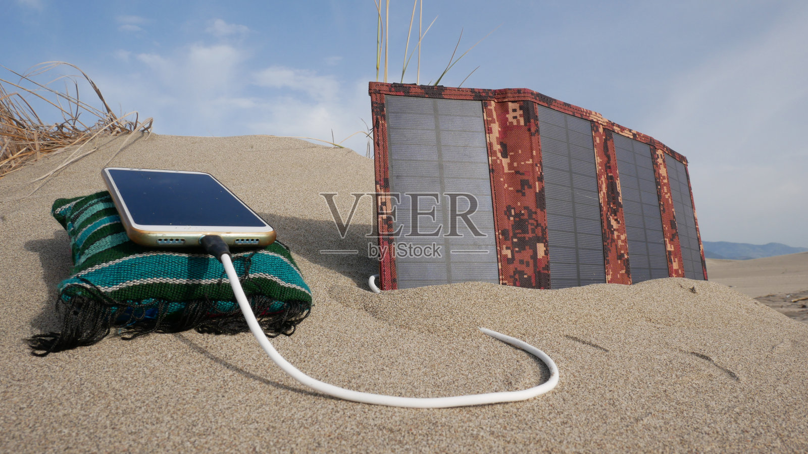 太阳能电池板以山脉为背景，在沙漠中为智能手机充电照片摄影图片