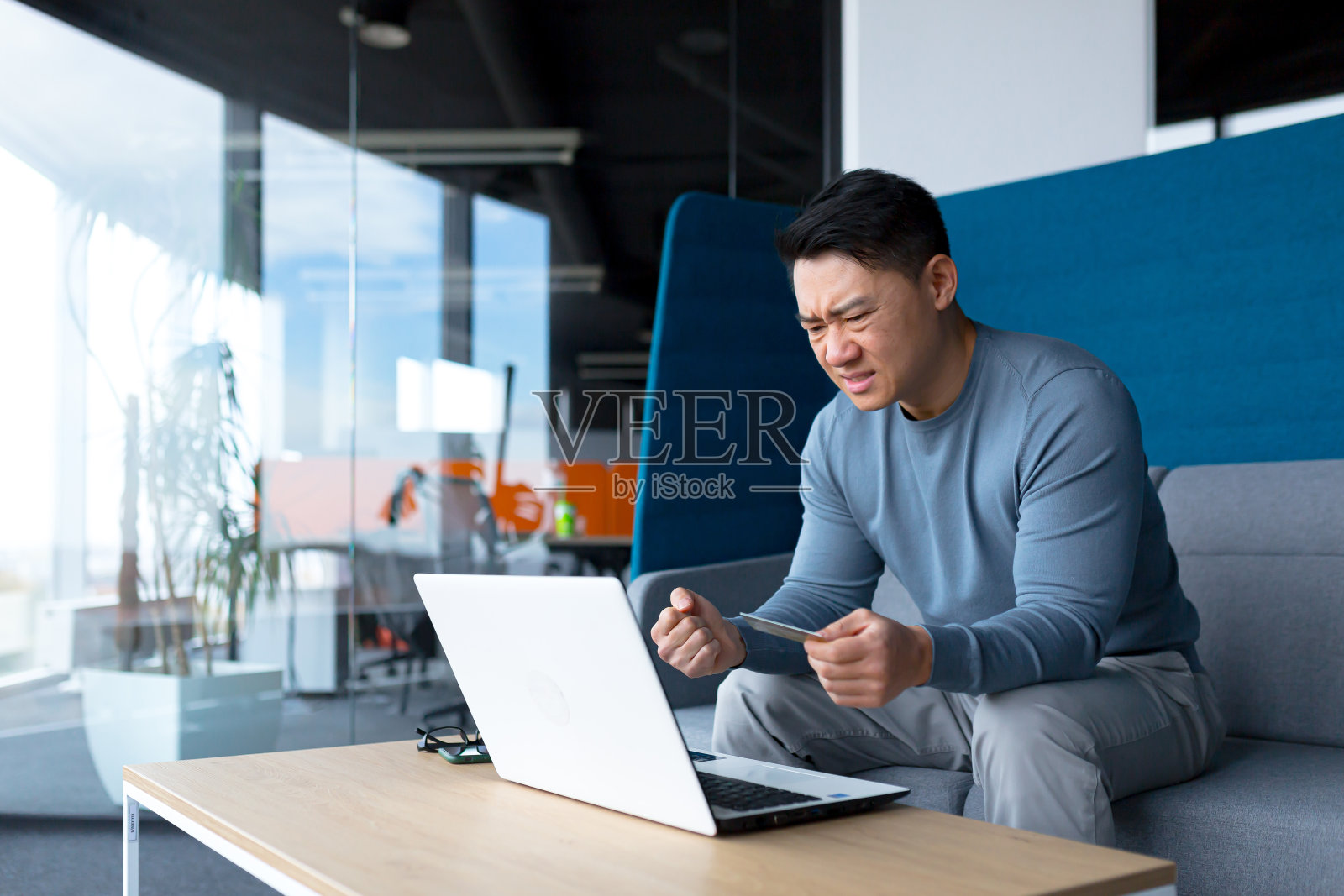 恼火的亚洲人试图用笔记本电脑和信用卡做银行业务，商人在现代办公室工作照片摄影图片