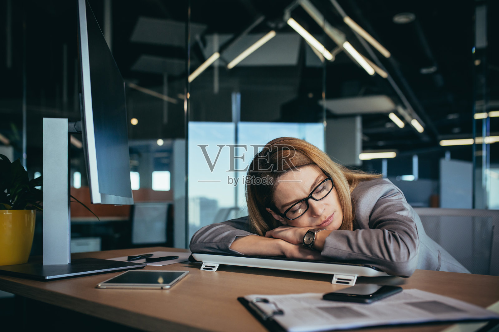 美丽的金发女商人在桌子上睡觉，在她的工作场所的电脑，在一个现代的办公室，工作到很晚，超负荷工作照片摄影图片