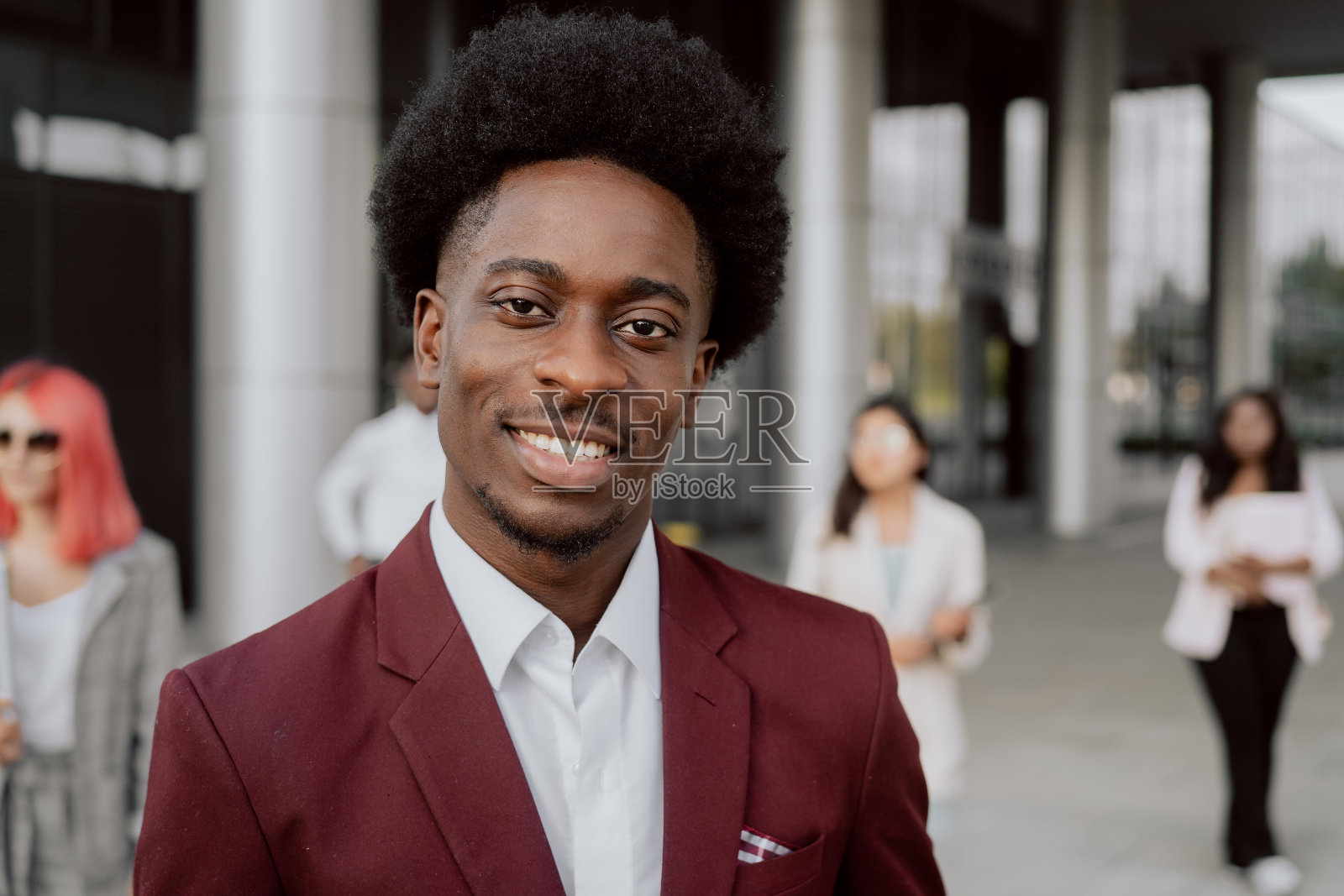 肖像男子顶着非洲式爆炸头，穿着栗色西装，男子是组长，经理，主管，主管，他站在公司大楼外面的背景员工照片摄影图片