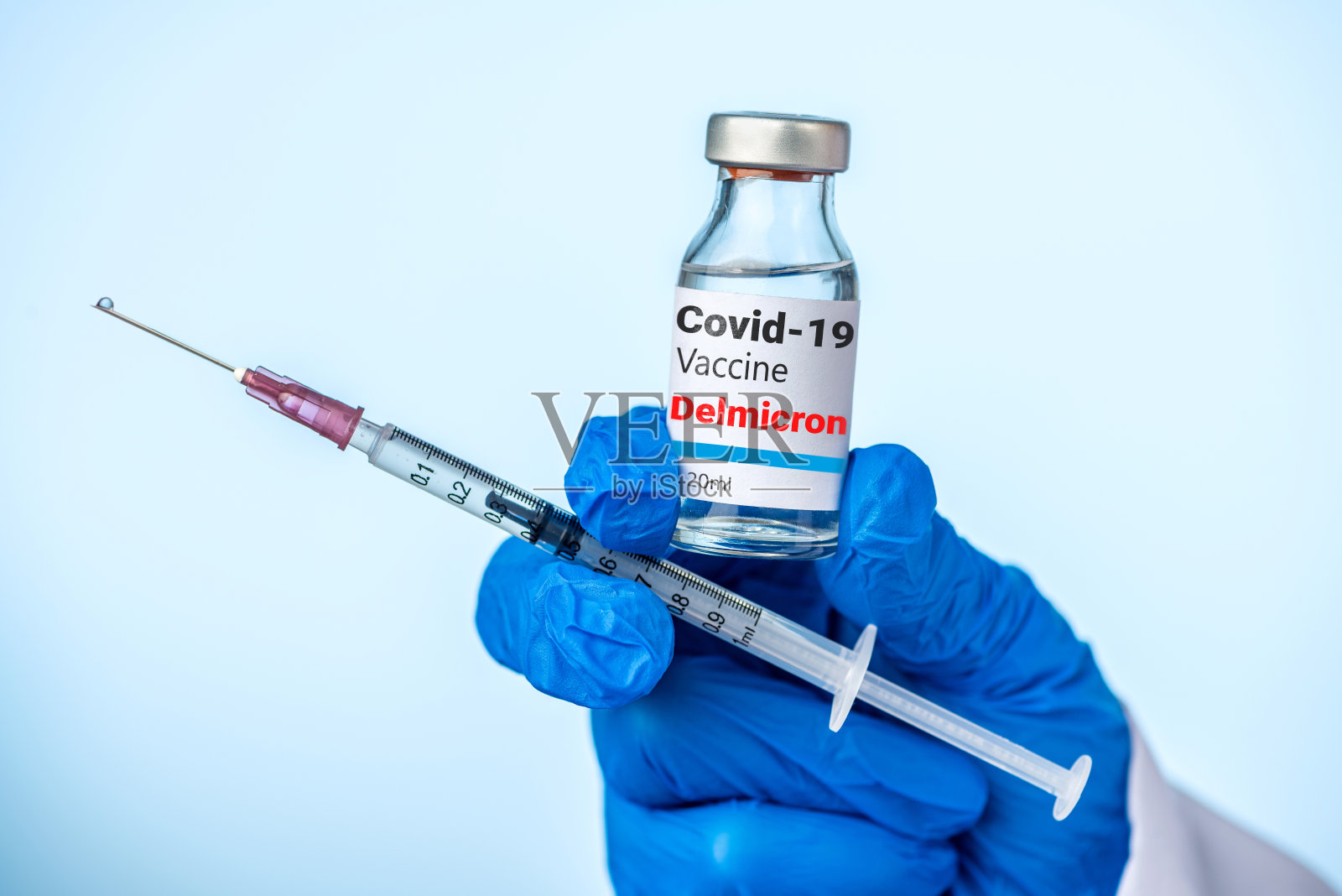 医生或护士用蓝色手套拿着Covid-19德尔米克隆变种疫苗和注射器。照片摄影图片