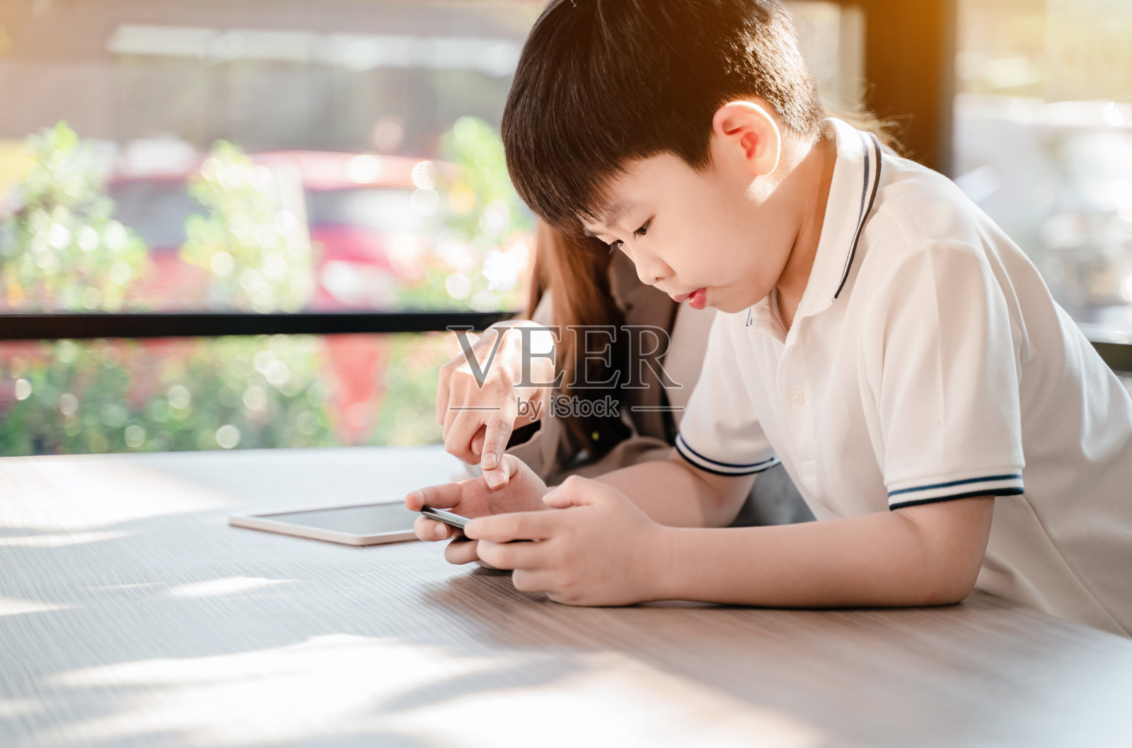 和孩子在咖啡厅工作的女商人。手机和数码平板电脑的亚洲家庭生活方式。照片摄影图片