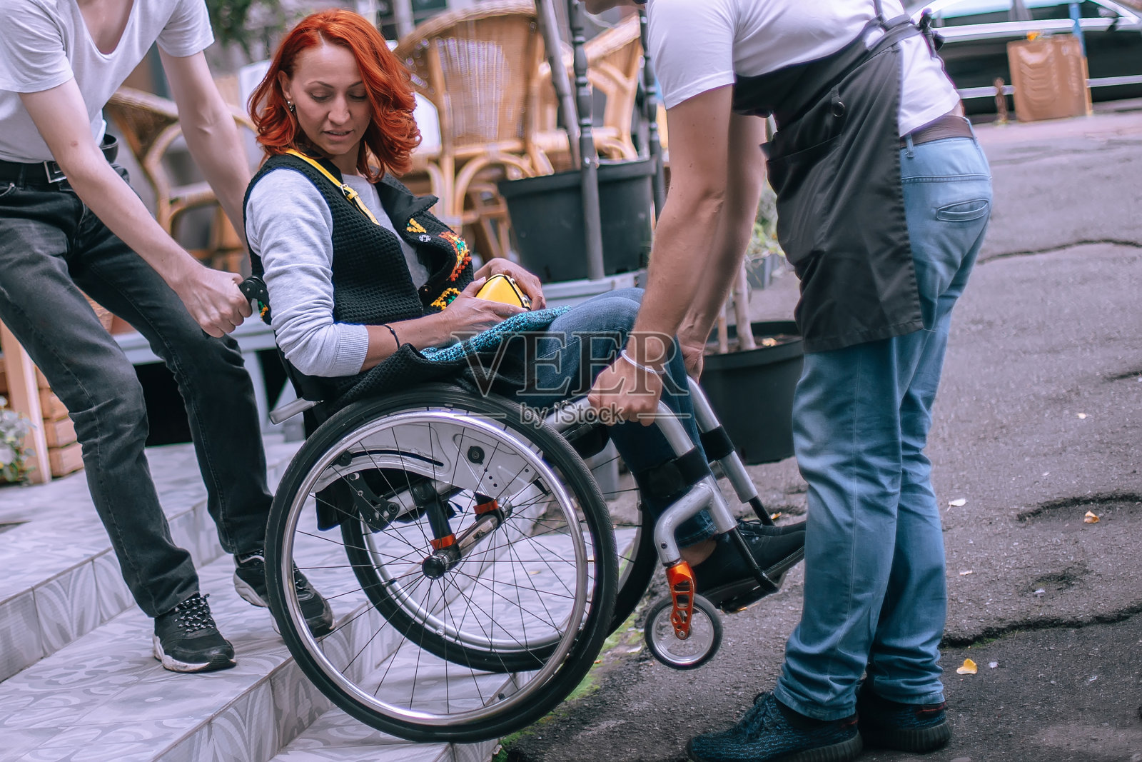 服务员用轮椅把一个女孩抬上没有斜坡的台阶。一位女士要去一家咖啡厅吃午饭，但有特殊需求的人是进不去的照片摄影图片