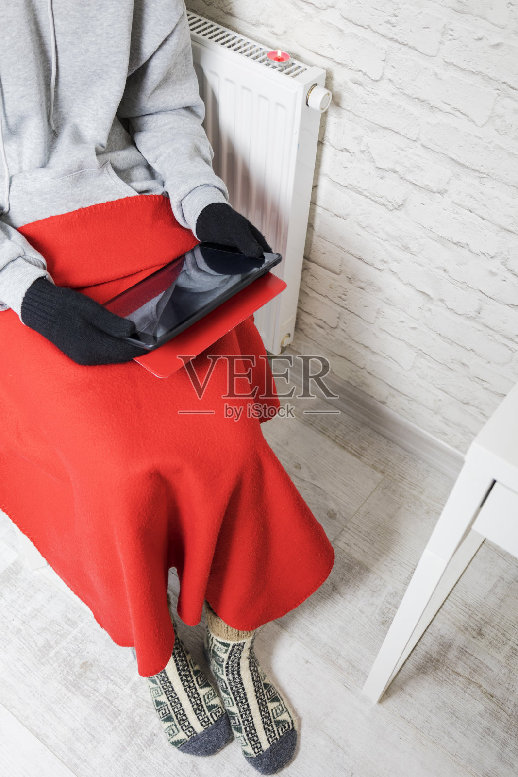 穿着暖和的袜子和手套的主人在暖气片旁取暖。严酷的冬天。加热的危机。照片摄影图片