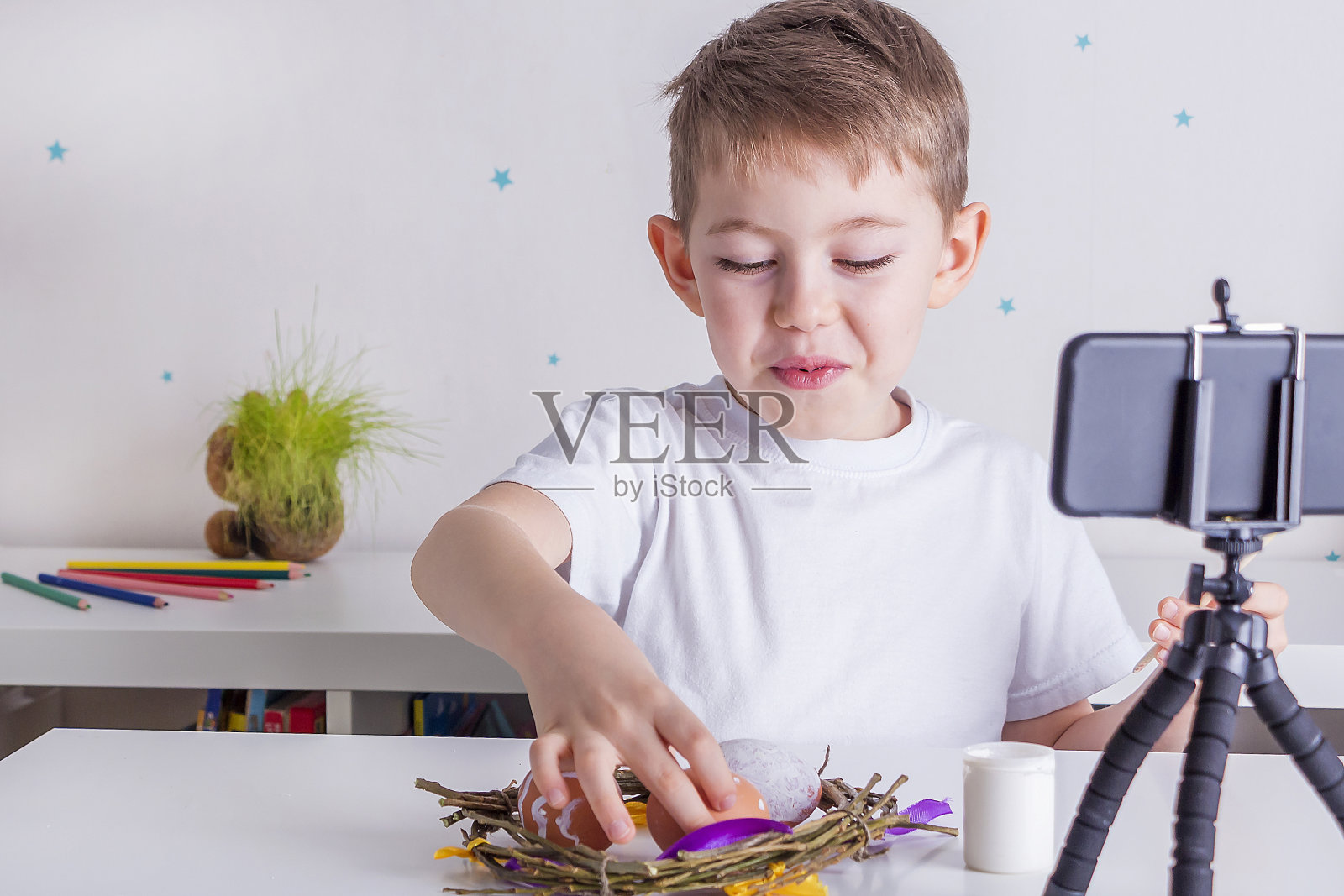 用智能手机直播视频的快乐小男孩博主。网上复活节大师班为追随者画彩蛋。博客概念，背光，选择性聚焦。照片摄影图片