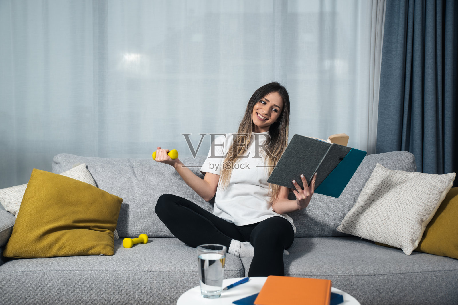 年轻快乐的健身女大学生坐在家里学习读书教育自己拿着小重量和锻炼一只手。健康向上的生活理念照片摄影图片